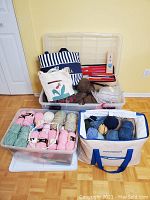 Large clear plastic bin holding dark brown yarn, smaller clear bin, striped tote and red needle case in background