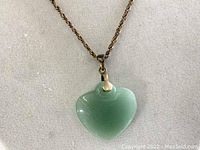 Close-up of jade heart-shaped pendant showing smooth polished light green surface with gold-tone bail attachment.
