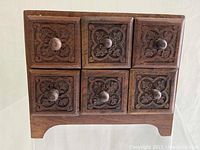 Front view of the carved wooden apothecary cabinet showing the 6 drawers with carved decorative faces and wooden knobs.