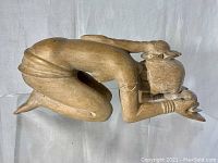 Side view of the wooden sculpture showing the woman kneeling and holding a flower with both hands.