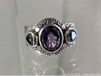 Close-up front photo of the silver ring showing three faceted stones and intricate metal scrollwork design.