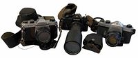 Three cameras lined up: Pentax K1000 (left), Nikon FE with long lens (center), silver-bodied SLR (right)