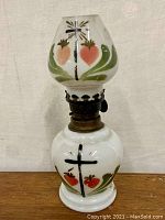 Front view of the porcelain lamp showing painted cross and heart motifs with leafy green designs.