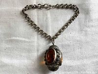 Sterling silver chain bracelet with large amber-colored faceted pendant on cream cloth background.