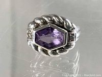 Front view of sterling silver ring with purple faceted stone and side stones on reflective surface.