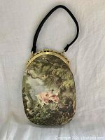 Front view of vintage silk purse showing the overall oval shape, metal frame, and print of a woman on a swing in a garden scene.