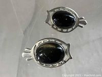 Pair of vintage Native American sterling silver earrings with black cat's eye stones placed on a clear surface, showing the oval shape and stylized cutouts on silver frames.