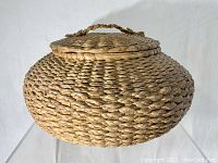 Side view of the round woven sweet grass basket with lid and braided handle showing the natural woven texture.