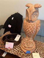 Beige owl statue and two bronze metal trays on leopard print fabric with a black coat in background