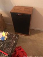 Single speaker front view showing wood veneer cabinet and black grille with Klipsch badge