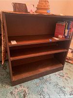 Full view of wooden bookcase with three shelves. Some books and items are on top and inside the bookcase but not included in the lot.