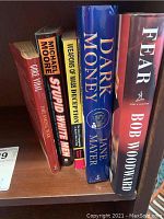 Spine view of five political books including titles by Bob Woodward, Michael Moore, Jane Mayer, and others, showing colors and titles clearly.