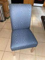 Front view of an upholstered dining chair with light blue fabric and pickled pine legs on tile floor.