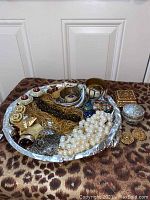 Overview of costume jewelry items on a silver plated tray and next to two small decorative boxes, showing various chains, earrings, faux pearl beads and bracelets.