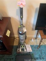 Full view of Hoover WindTunnel Air upright vacuum cleaner standing on carpet beside furniture, showing overall item and power cord.