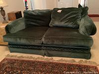Front view of green velour love seat showing two seat cushions, four back cushions, and braided trim along base.