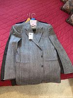 Grey pinstripe men’s suit jacket stacked on top of other dark-colored jackets on red bedspread