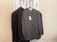 Four men's jackets hung on hangers on a wall-mounted rack, including a gray Ungaro suit and others darker in color.