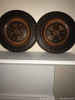 Pair of round wooden plates displayed side by side showing engraved floral and geometric patterns with colorful paint accents