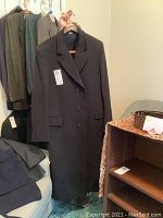 Full front view of long black men's wool coat on hanger with buttons fastened, showing its full length and style.