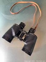 Front view of the Bushnell antique binoculars with textured black body and tan leather neck strap.