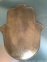 Front view of the brass Hamsa hand showing detailed engraved eye and floral pattern.