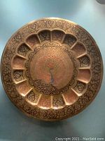 Top view of the round brass tray showing embossed floral patterns and a colorful hand-painted peacock in the center with orange, green, and red details.