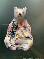 Front side of the ceramic bear figurine showing the hand-painted snowy landscape with trees and a cabin.