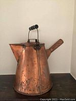 Front and side view of the antique copper kettle showing its spout, textured handle and black handle grip on metal top handle.