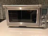 Front view of closed Breville stainless steel toaster oven with glass door and control panel on the right.