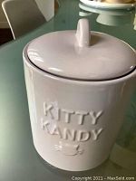 White ceramic pet snack container with lid and embossed 'KITTY KANDY' text on front, shown closed.