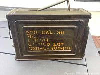 Side view showing the olive green metal box with yellow stenciled military markings and lot number.