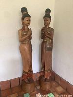 Two full statues of Balinese praying ladies standing side by side at corner, showing front view and bases.