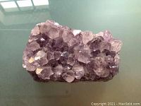 Purple amethyst crystal cluster with pointed crystals on a flat reflective surface showing side and top views in two photos.