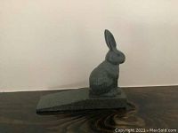 Side view of the bronze rabbit door stopper sitting on a wooden surface.