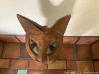 Close up of carved wooden cat head showing stylized cat face, eyes, nose, and ears