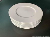 Stack of six white large charger plates with wide rim visible.