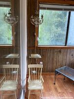 Overall view of chandelier, child's chair and metal side table on porch with wood panel walls and windows.