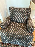 Front view of upholstered armchair with patterned fabric, showing loose cushions and cylindrical armrest cushions.