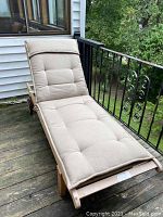 Full view of wooden chaise lounge on outdoor deck with tufted beige Sunbrella cushion and slightly elevated headrest.