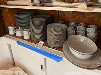 Shelved display of two stacks of dinner plates, bowls, cups, and saucers showing the Noritake China with pastel floral rims