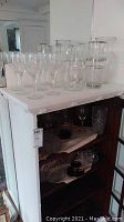Wide shot showing multiple clear cut glass wine glasses, pitchers, decanter on white surface