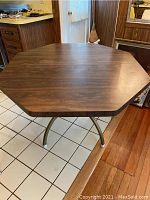 Full view of the octagonal wood grain kitchen table with metal legs showing wear and surface condition.