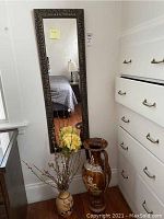 Full view of mirror mounted on the wall with ornate dark brown plastic frame, tall and narrow shape.