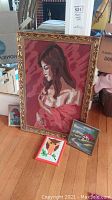 Framed needlepoint portrait of woman with brown hair and red shawl, large ornate gold frame, and two smaller framed needlepoint pieces showing a fox and a rural landscape.