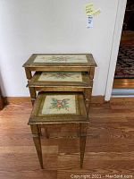 Front view of the stacked three Florentia nesting tables showing gold gilt finish and floral tile tops.