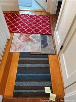 Four scatter rugs arranged on hardwood floor in hallway showing the various patterns and colors, including red lattice pattern, blue stripes and two smaller abstract designs.
