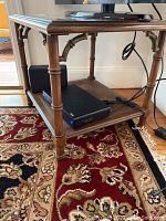 Side view of the side table showing faux bamboo style legs, lower caned shelf, and visible wear on wood finish.