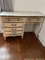 Photo showing full desk from front with cream color, ornate top, curved legs, and multiple drawers.