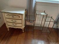 Nightstand and metal plant stand side by side on hardwood floor near window.